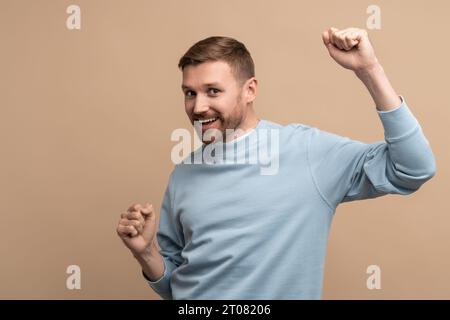 Overjoyed happy man showing win victory gesture on beige background looking at camera. Stock Photo