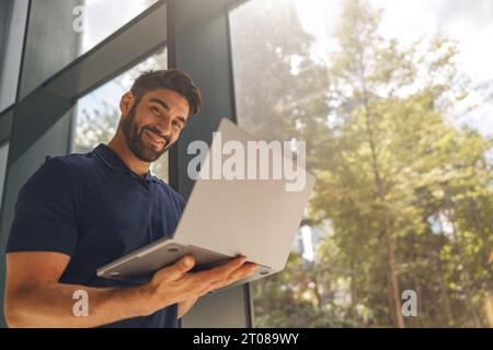 Smiling entrepreneur working on laptop standing in coworking during working day and looks camera Stock Photo