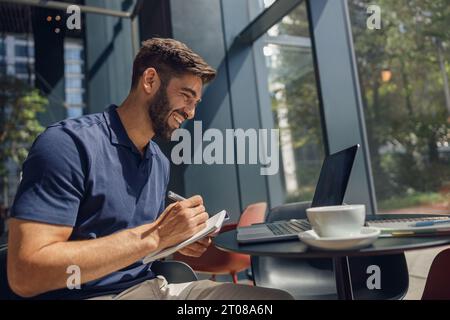 Smiling businessman have a business meeting via video call sitting in cafe and making notes Stock Photo