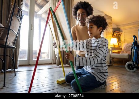 African american single mother with son drawing on board with chalks together. Family love concept. Stock Photo