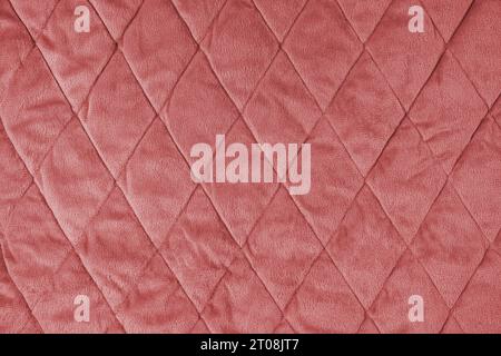 Quilted velours fabric background. Red texture blanket or puffer jacket, stiched with diamond pattern, soft wrinkled surface, crupmed textile Stock Photo