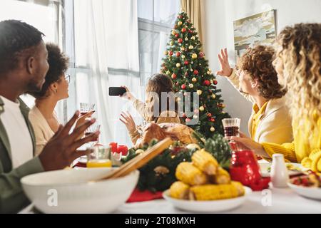 big multicultural family gesturing and taking selfie at holiday table with wine and food, Christmas Stock Photo