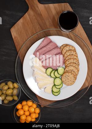 Top view of a simple, rustic table serving cheese, salami, and crackers along with olives, ground cherries, and cucumbers. Stock Photo