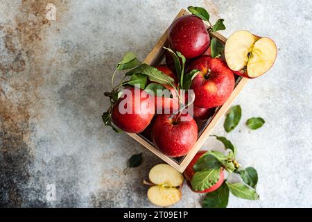 Top view of whole fresh red ripe organic delicious apples with green leaves filled in wooden box with half cut pieces and placed on gray surface in da Stock Photo