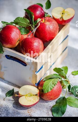High angle of whole fresh red ripe organic delicious apples with green leaves filled in wooden box with half cut pieces and placed on gray surface in Stock Photo