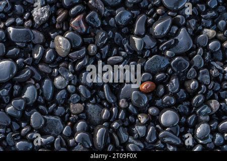 Top view of wet stones located near smooth sedimentary rock on coast in Reynisfjara Beach Stock Photo
