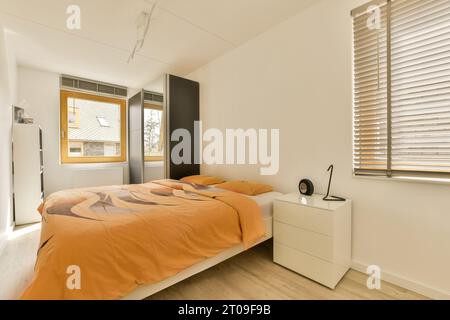 Interior of bedroom with orange sheet and pillows on bed in front of white wall at home Stock Photo