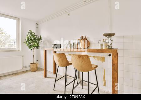 Kitchenware with clock and small plants on wooden table with empty chairs in kitchen with white walls at apartment Stock Photo