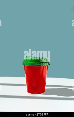 Minimalist red plastic cup of takeaway coffee and green lid against blue background Stock Photo