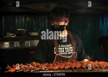A chef makes a Thai barbecue grill filled with meat skewers on the night street food market.  The delicious smells and flavors attract hungry customers at the market. (Photo by Daniil Kiselev / SOPA Images/Sipa USA) Stock Photo