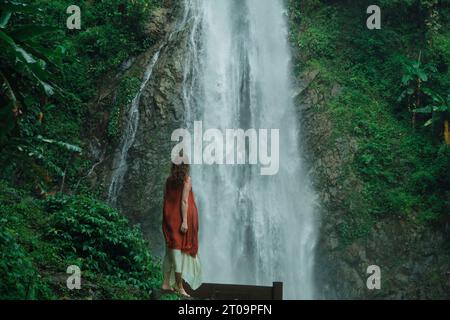 A girl dressed in a vibrant red and white outfit stands in front of a mighty waterfall in the jungles. (Photo by Daniil Kiselev / SOPA Images/Sipa USA) Stock Photo
