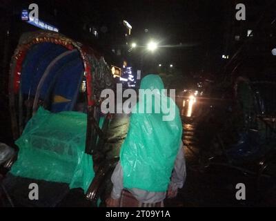 Dhaka, Bangladesh. 5th Oct, 2023. A rickshaw puller waits for passengers while using a plastic sheet to shield them from the rain. The capital's daily life was reportedly disrupted by a continuous rain depression. (Credit Image: © MD Mehedi Hasan/ZUMA Press Wire) EDITORIAL USAGE ONLY! Not for Commercial USAGE! Stock Photo