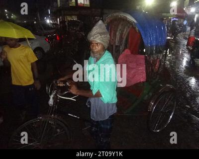 Dhaka, Bangladesh. 5th Oct, 2023. A rickshaw puller waits for passengers while using a plastic sheet to shield them from the rain. The capital's daily life was reportedly disrupted by a continuous rain depression. (Credit Image: © MD Mehedi Hasan/ZUMA Press Wire) EDITORIAL USAGE ONLY! Not for Commercial USAGE! Stock Photo