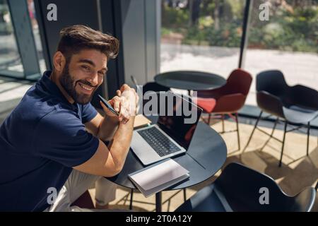 Handsome smiling entrepreneur working on laptop sitting in coworking during working day Stock Photo