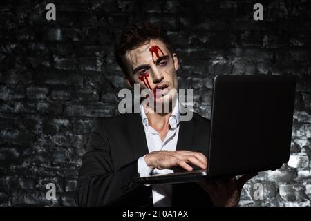 Tired zombie manager working on laptop in dark studio Stock Photo