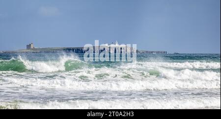 Panoramic view of Inner Farne lighthouse and St Cuthbert's church on the Farne Islands through crashing waves on Bamburgh beach, Northumberland, UK, o Stock Photo