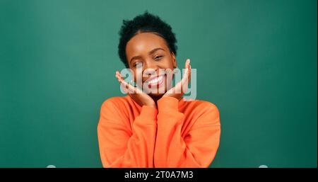 Beautiful Black woman cups hands under chin in cute pose, green studio Stock Photo