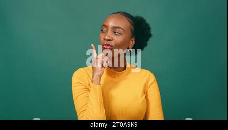 Serious young woman taps chin while thinking, contemplating, green studio Stock Photo