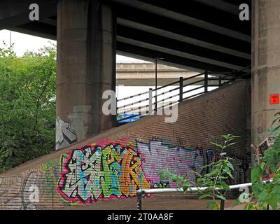 colourful graffiti on brick wall and concrete supporting pillar of modern bridge over inland canal in shadows - England, UK Stock Photo