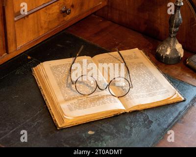 Still life of open book with old German writing, round reading glasses and candlestick on antique secretary Stock Photo