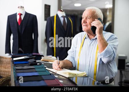 Professional tailor man talking on mobile phone and making notes in notebook Stock Photo