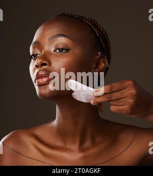 Woman, facial and gua sha in hand on studio background for mockup in beauty, treatment or skincare. Black person, model or massage for glow, lymphatic Stock Photo