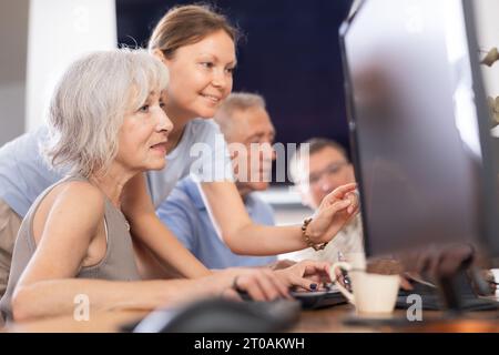 Old woman learning computer programs with teacher in training room Stock Photo