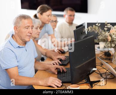 Focused older gentleman using computer at internet cafe Stock Photo