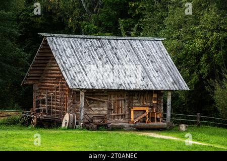 Old wooden barn log house with a wooden roof on a background of green forest Stock Photo