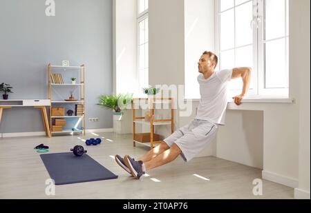 Fit, strong man doing triceps dips by window sill during fitness workout at home Stock Photo