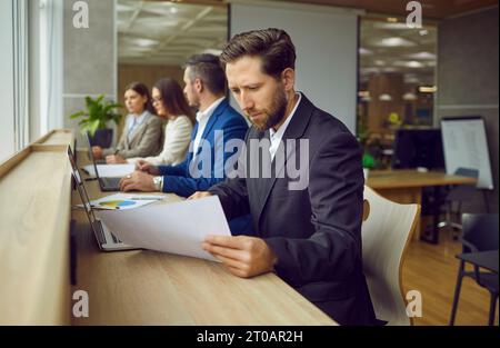 Man working in office, doing business research, reading paper report, and using laptop computer  Stock Photo