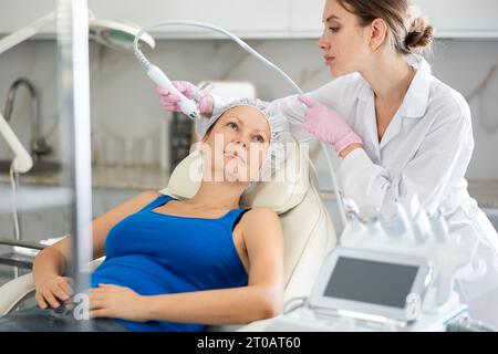Beautiful female doctor making facial gas-liquid oxygen water epidermal peeling using macromolecule atomizing pen  Stock Photo
