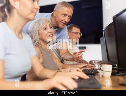 Old woman learning computer programs with teacher in training room Stock Photo