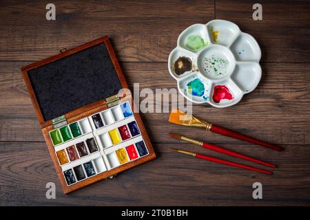 A ceramic watercolor palette and paints and brushes on a rustic wooden background Stock Photo