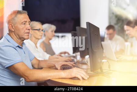 Focused older gentleman using computer at internet cafe Stock Photo