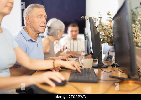 Concentrated elderly man immersed in using computer in library Stock Photo