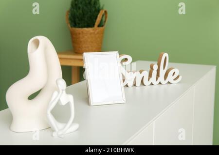 Blank frame and decor on white sideboard near green wall Stock Photo