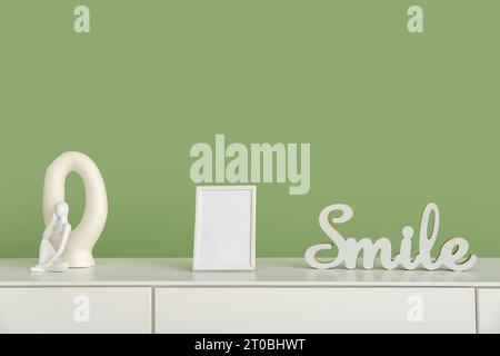 Blank frame and decor on white sideboard near green wall Stock Photo