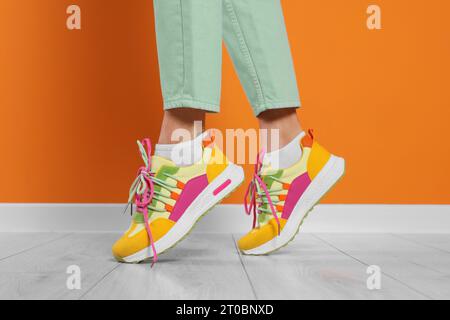 Woman wearing pair of new stylish sneakers near orange wall, closeup Stock Photo