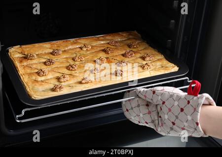 Woman taking baking pan with delicious pie from electric oven in