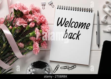 Notebook with phrase Welcome Back, bouquet of flowers and stationery on white wooden table, flat lay Stock Photo