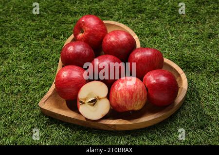 Wooden plate in shape of heart with red apples on green grass Stock Photo