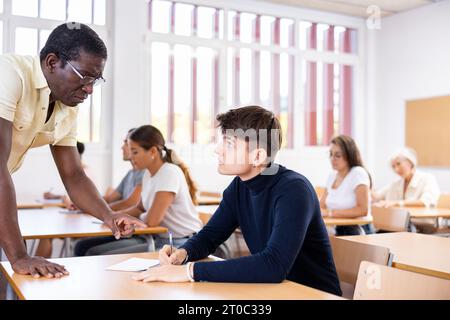 Professor explaining task solution to young man in college Stock Photo