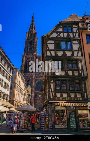 Strasbourg, France - May 31, 2023: Facade and the spire of Notre Dame Cathedral and ornate traditional half timbered houses with steep roofs around it Stock Photo