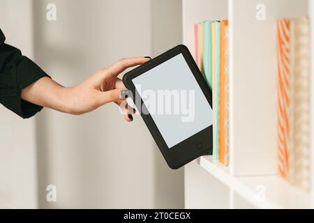 Man taking modern e-book reader from a bookshelf close up Stock Photo