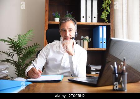 Man working as a team virtually taking notes in online meeting with a laptop in the home office Stock Photo