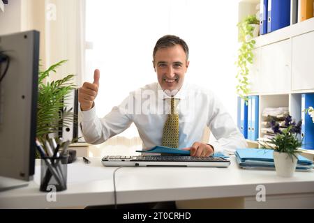 Happy smiling freelance worker in white shirt and tie making ok sign with hand looking straight working in white office with folders. Stock Photo