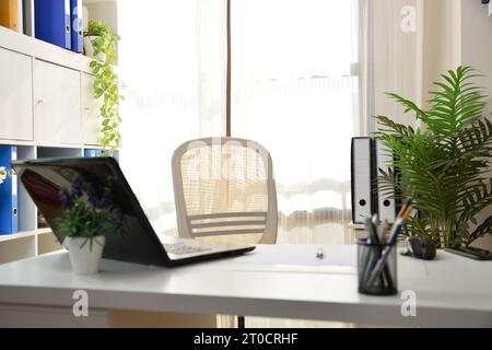 Detail of office with white furniture with folders on table and shelves and laptop without people. Stock Photo
