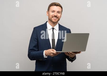 Positive man trader, crypto investor, entrepreneur, financier holds laptop on gray background. Stock Photo