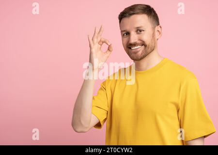 Positive happy man showing OK sign hand gesture on pink background looking at camera. Stock Photo